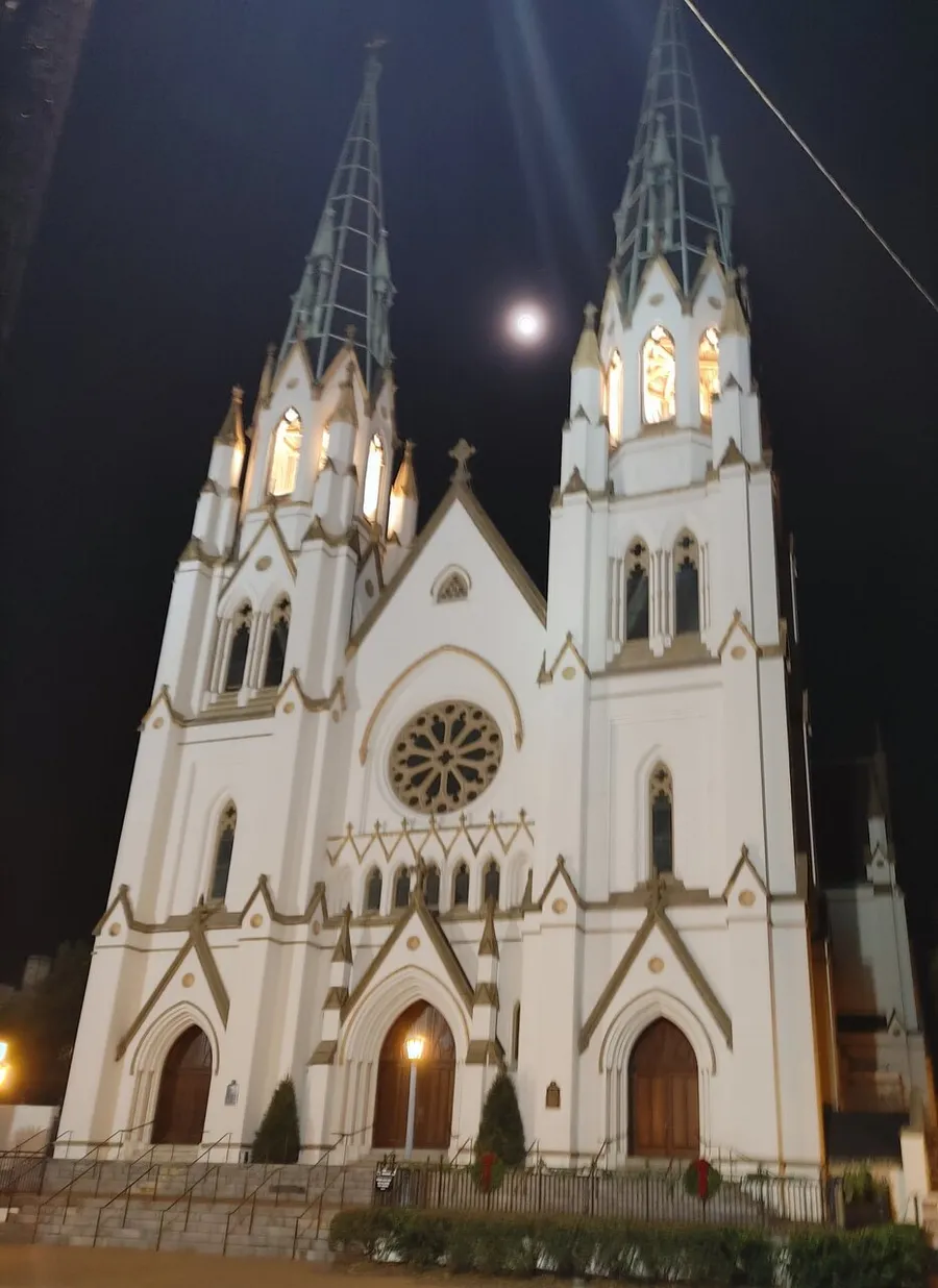 A nighttime photograph displays the illuminated facade of a Gothic-style church with twin spires under a moonlit sky.