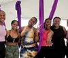 A group of smiling people are using purple aerial silks in a fitness studio with one person doing an upside-down pose