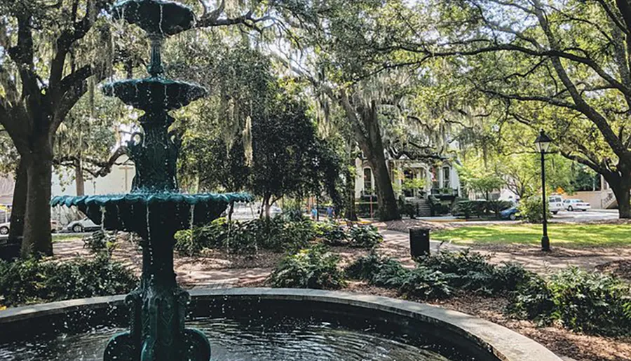 This image showcases a tranquil park scene with an ornate fountain in the foreground, surrounded by lush greenery and draped Spanish moss, conveying a sense of Southern charm.