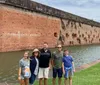 A group of five people stands smiling in front of an old brick fortification surrounded by a moat