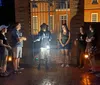 A group of people is listening to a guide who is holding a lantern during what appears to be an evening or night tour outside a gated brick building