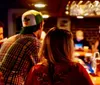 Patrons are gathered at a dimly lit bar with some engaged in conversation and a bartender wearing a face mask suggesting the photo was taken during a time of health precautions