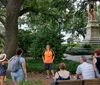 A person in an orange and blue outfit is speaking to a group of attentive listeners in an outdoor setting