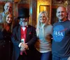 The image shows five people smiling for a group photo with one man in a top hat and red tie standing in the center