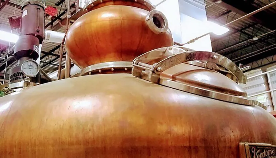 The image shows the shiny copper components of a distillery setup, likely used for making spirits such as whiskey or rum, housed within an industrial environment.