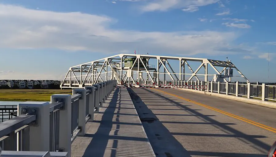 The image shows a steel truss bridge with a pedestrian sidewalk under a clear blue sky.