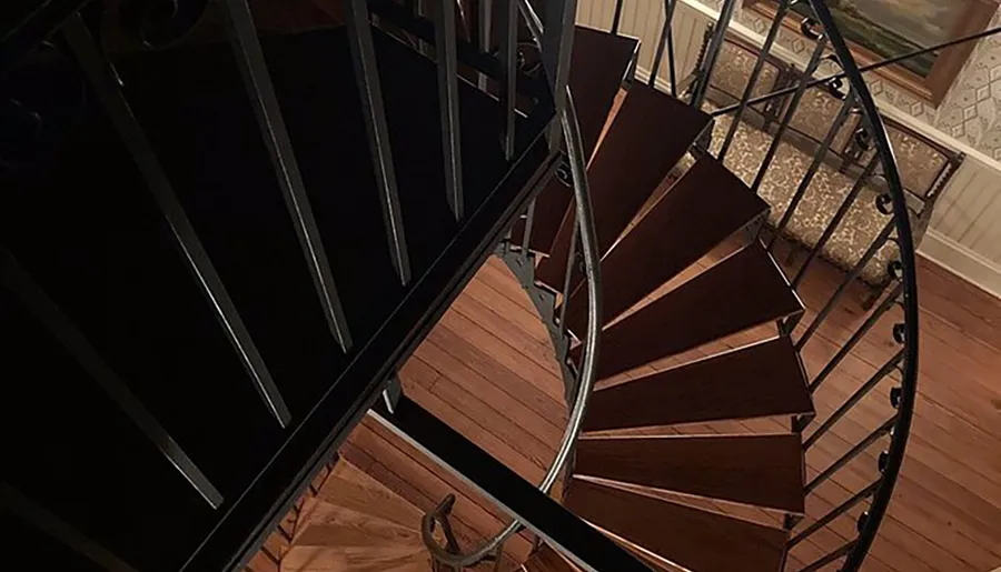 This image shows a top-down view of a wooden spiral staircase with wrought-iron railings inside a house.