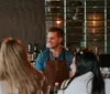 A bartender in an apron is engaging with patrons at a bar with a stylish hexagonal tile backdrop