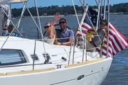 A group of people is enjoying a sunny day sailing on a boat adorned with the American flag.