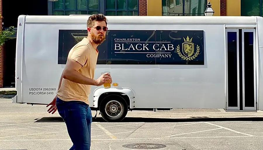 A man in sunglasses is walking past a white shuttle van with Charleston Black Cab Company branding.