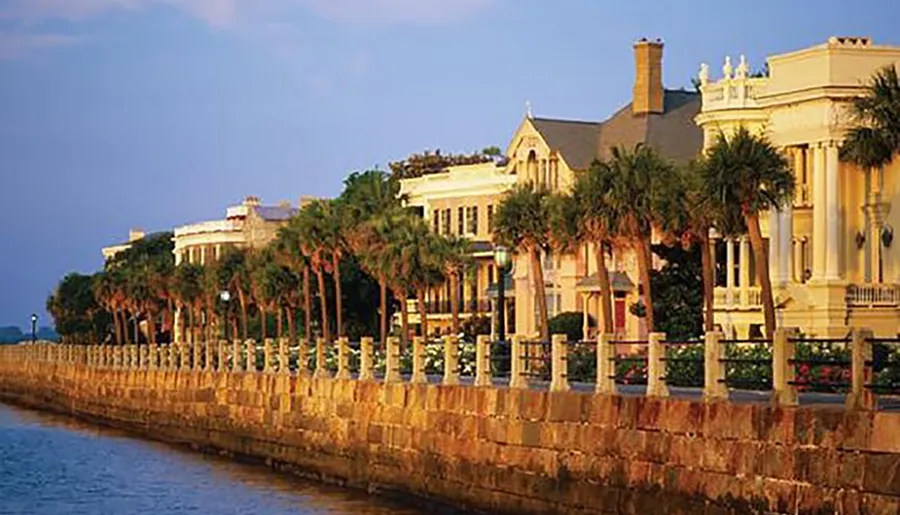 The image shows a picturesque row of palm-lined stately homes along a seawall at dusk, reflecting a coastal charm likely characteristic of a historic southern town.