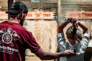 A man is instructing a woman on how to throw an axe at an indoor axe-throwing venue.