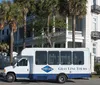 A Gray Line tour bus is parked on a sunny street lined with palm trees in front of an elegant building with balconies