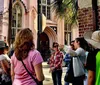 A group of people is participating in an outdoor tour near a historical building with a guide gesturing and explaining something of interest