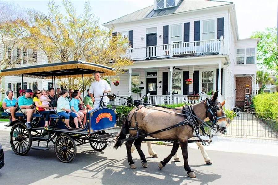 A horse-drawn carriage with passengers is being led by a driver through a quaint street with traditional houses.