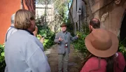A tour guide is explaining something to a group of visitors in a picturesque outdoor setting.