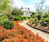 A brick pathway meanders through a vibrant garden leading to a classic white house with large columns