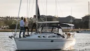 Three people and a dog are enjoying time on a sailboat near the shore during the late afternoon.