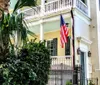 A traditional American flag hangs from the balcony of a charming pastel-colored house with shutters nestled amidst lush greenery