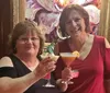 Two smiling women are toasting with cocktails in front of a vibrant abstract painting