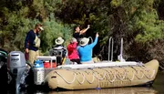 A group of people enjoy a guided tour on a large inflatable boat on a calm river, surrounded by woodland.