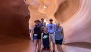A group of tourists is posing for a photo inside a narrow, curved, orange sandstone slot canyon.