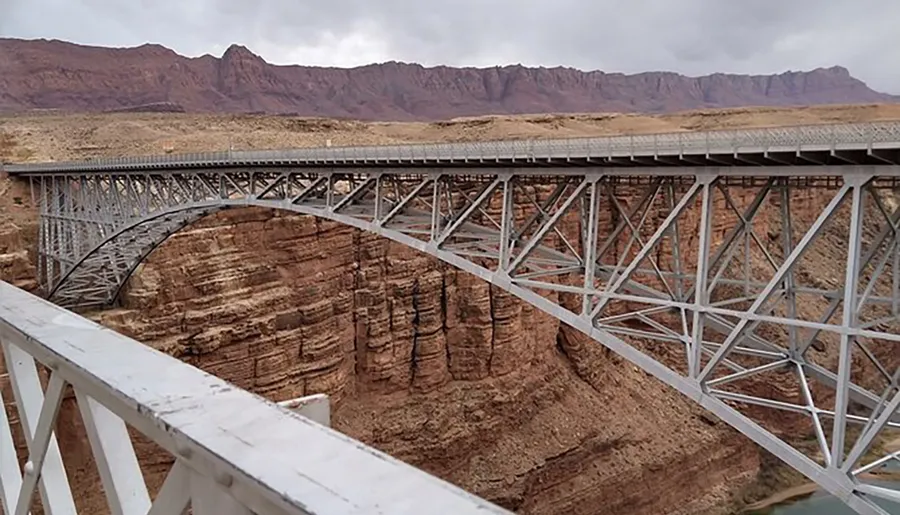 The image features a large steel arch bridge spanning a deep canyon with rugged terrain in the background, symbolizing impressive engineering amidst natural beauty.