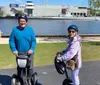 Two people on Segways are posing next to a large metal statue of a bear by a lakeside