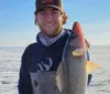 A person is holding a large fish with a snowy landscape and ice in the background indicating ice fishing success