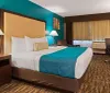 The image shows a well-appointed hotel room with a large bed vibrant teal and brown decor a desk with a chair a television and patterned carpeting