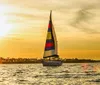A sailboat with a colorful sail glides over the water against a stunning sunset backdrop