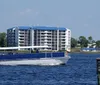 A blue and white tour boat is cruising along a waterway with a multistory building in the background under a clear blue sky