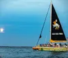 The image shows a colorful catamaran with a group of people on board sailing on calm waters during a beautiful sunset