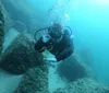 A scuba diver gives an OK hand signal while exploring underwater near some rocky formations on the ocean floor