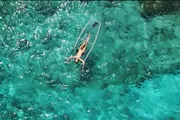 A person is lying on a paddleboard in the middle of clear, turquoise waters.