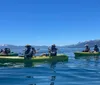 A group of people are kayaking on calm blue water with a backdrop of majestic snow-capped mountains under a clear blue sky