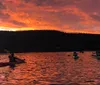 A group of kayakers paddle on a lake under a vivid orange sunset sky