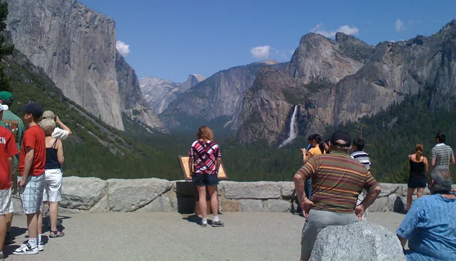 Visitors are enjoying the view of a scenic mountain landscape with waterfalls from an overlook point.
