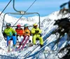 Skiers in colorful attire are seated on a chairlift against a backdrop of snow-covered mountains
