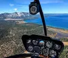 The image shows the cockpit view from a helicopter flying over a scenic landscape with a large lake and mountainous terrain in the background