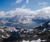 The image showcases a panoramic alpine landscape featuring snow-capped mountains and a series of lakes nestled among the rugged terrain under a partly cloudy sky