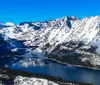 The image showcases a panoramic alpine landscape featuring snow-capped mountains and a series of lakes nestled among the rugged terrain under a partly cloudy sky