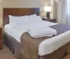The image shows a neatly made hotel room bed with white linens and a brown bedspread flanked by matching nightstands with lamps