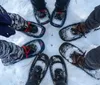 A group of people wearing snowshoes are standing on snow forming a circle with their feet pointing towards the center