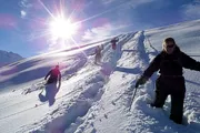 A group of hikers ascends a snowy slope under a bright sun.