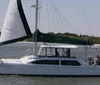 A catamaran named Howling Owl is sailing near a coastline with its sails partially unfurled in calm waters