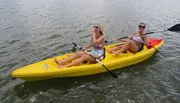 Two people are enjoying paddling in a yellow kayak on a body of water.