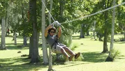 A person is enjoying a zipline adventure in a lush green park.
