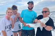 A group of people on a boat are smiling and posing with a small shark that one man is holding.