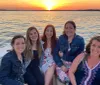 Five smiling individuals are enjoying a scenic boat ride during a beautiful sunset over a calm sea